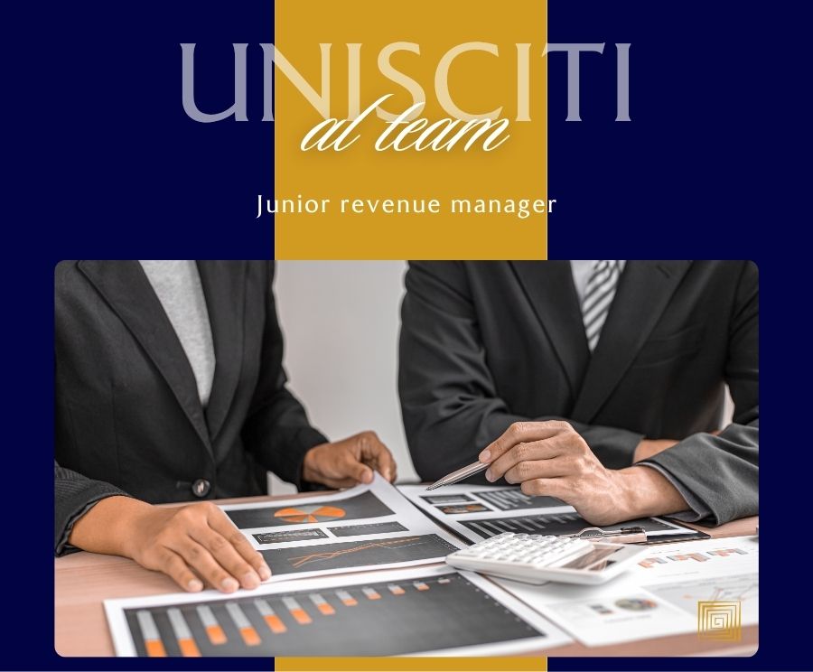 Due persone in abiti formali sedute a una scrivania esaminano documenti e grafici, con una calcolatrice sul tavolo; sullo sfondo si vede un logo blu e giallo con la scritta Unisciti al team e la dicitura Junior revenue manager.