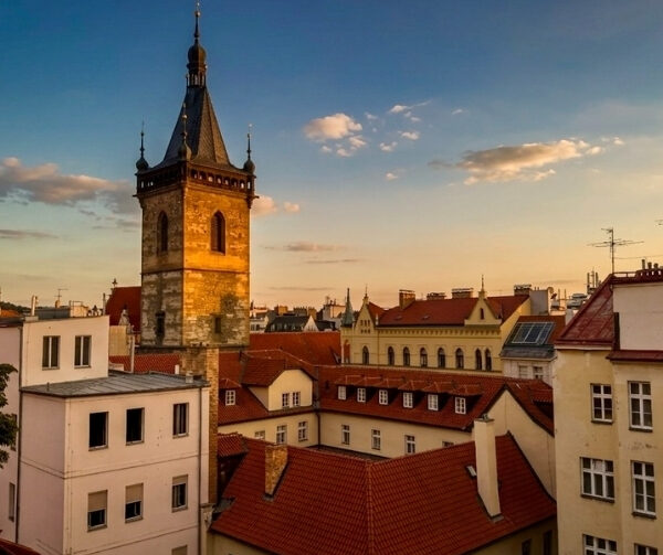 Veduta di una città con tetti rossi e una torre della chiesa alta, al tramonto, sotto un cielo azzurro con alcune nuvole.