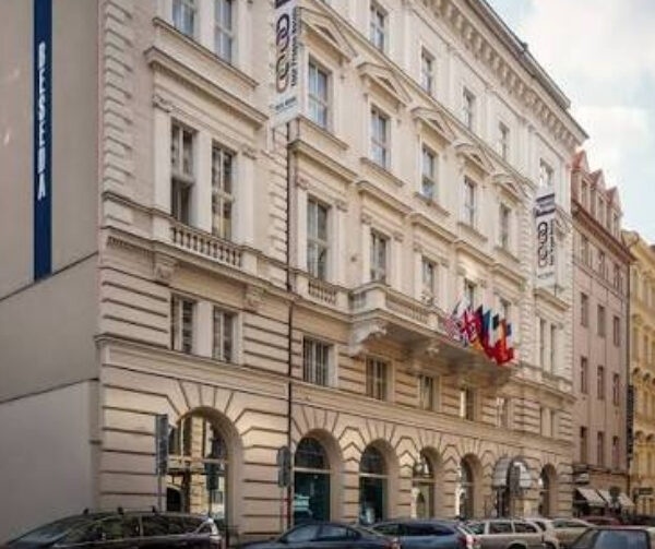 Edificio storico in stile classico su una strada cittadina, con facciata ornata, archi al piano terra e finestre alte; bandiere appese alla facciata e diverse auto parcheggiate lungo la strada.