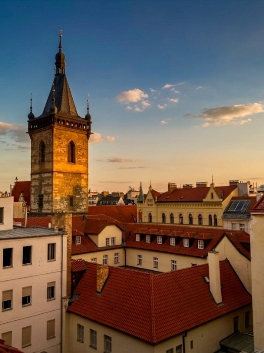 Veduta di una città europea con tetti rossi in coppi e una torre campanaria in pietra, al tramonto.