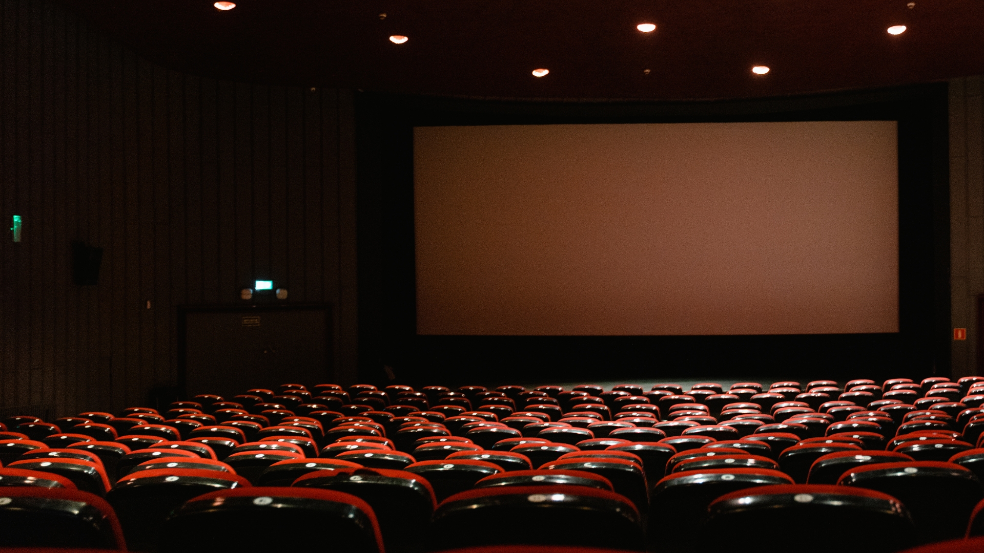 An empty movie theater with rows of red seats facing a large screen.