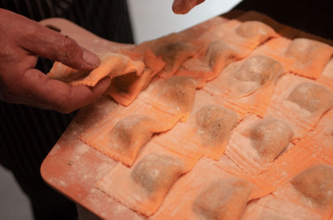 Eine Person formt orangefarbene Teigtaschen (Ravioli) auf einem mit Mehl bestäubten Backblech.