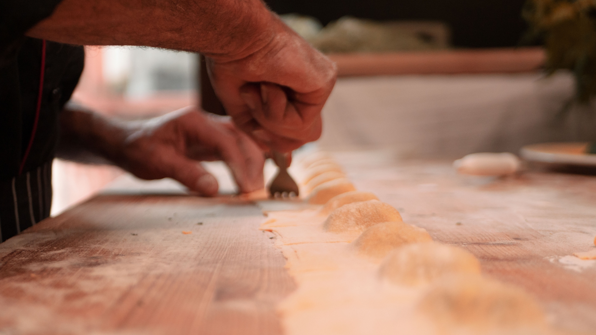 Le mani di una persona modellano una fila di piccoli pezzi di impasto su una superficie di legno, usando una forchetta.