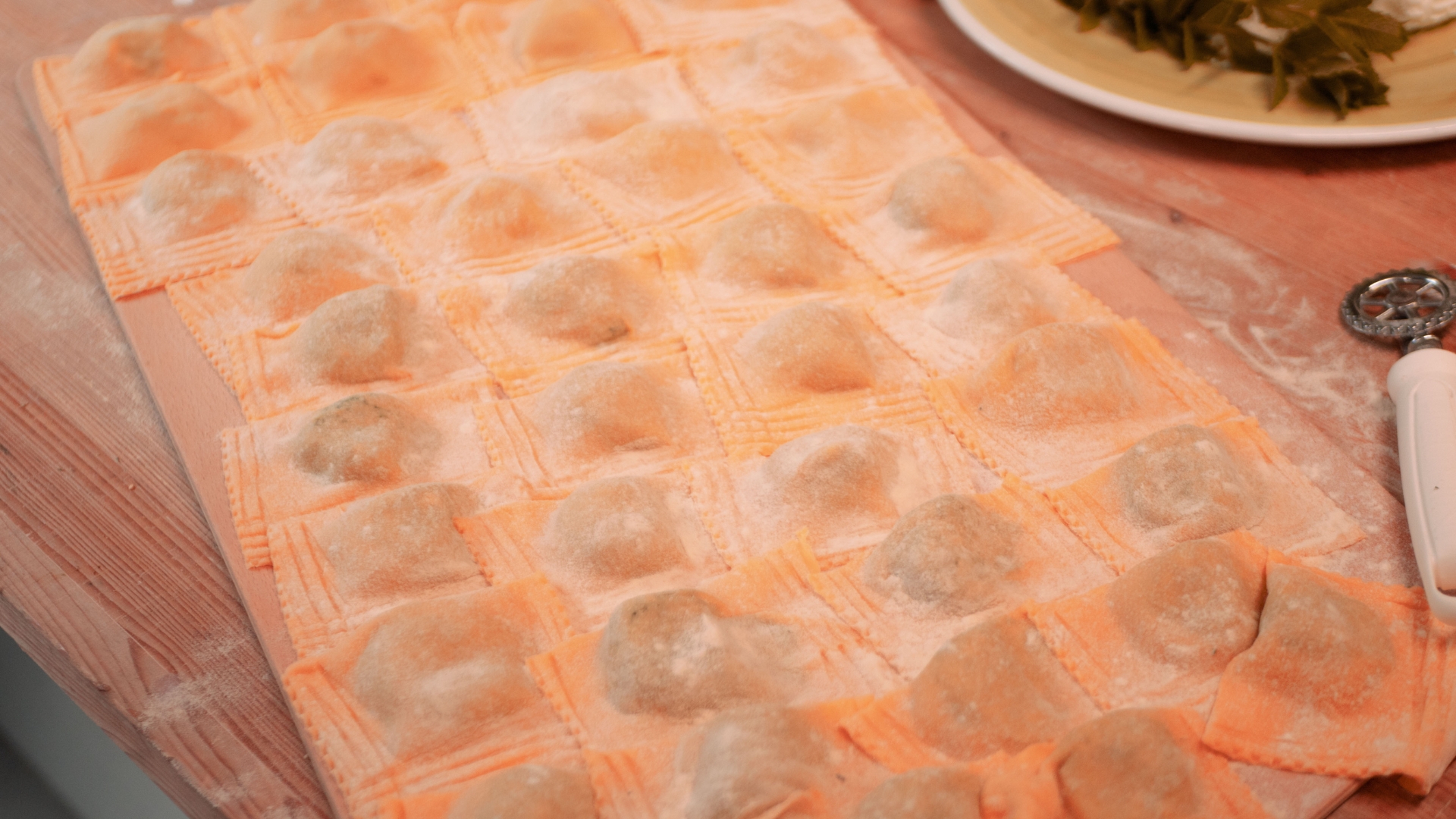 Foglio di pasta arancione steso sul tavolo, tagliato in piccoli ravioli o gnocchi infarinati, pronti per la cottura.