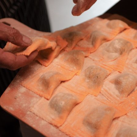 Close-up of hands shaping orange ravioli on a flour-dusted surface, arranged in rows with visible filling.